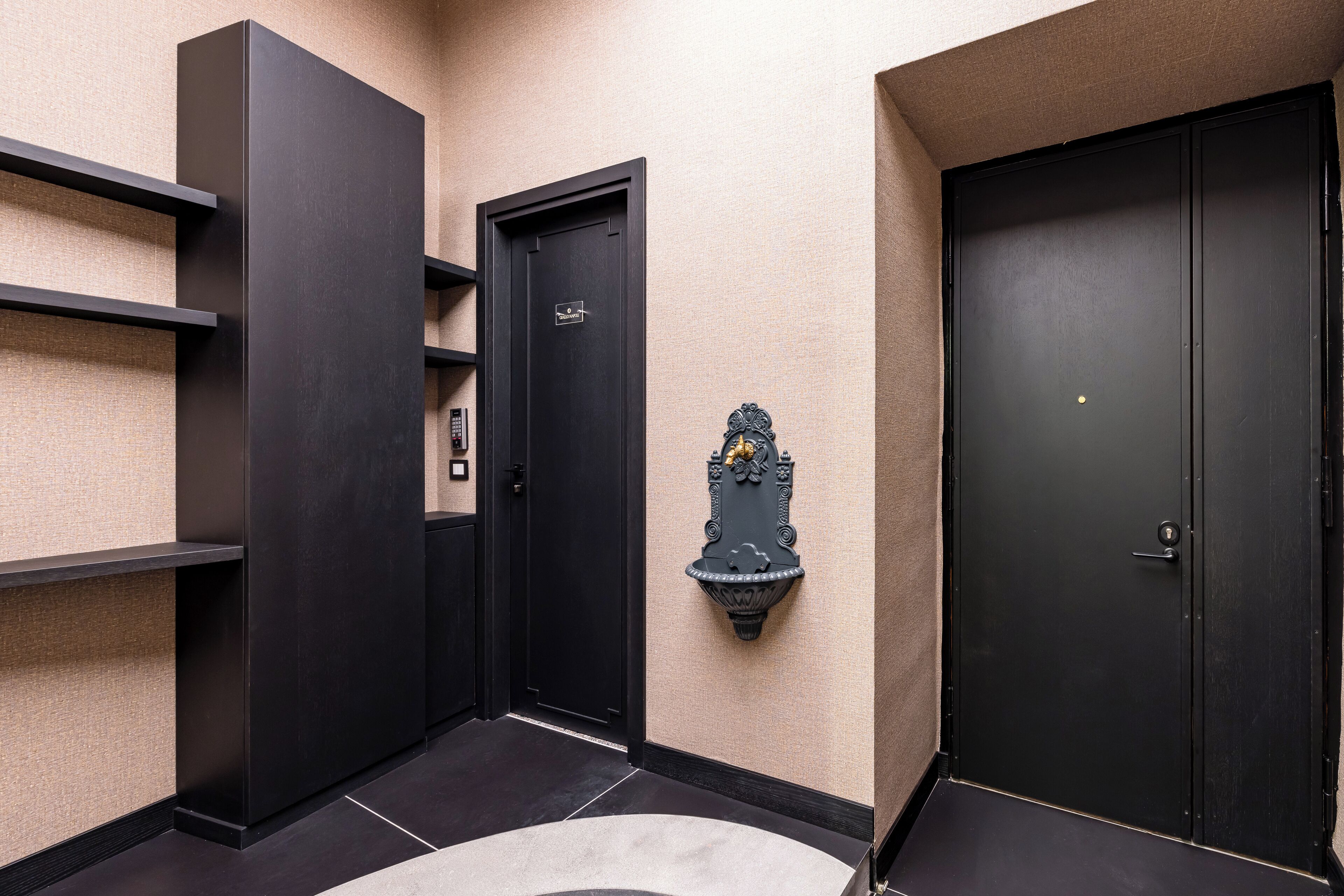 A hallway with dark wooden doors, a wall-mounted light fixture, and a textured wall.