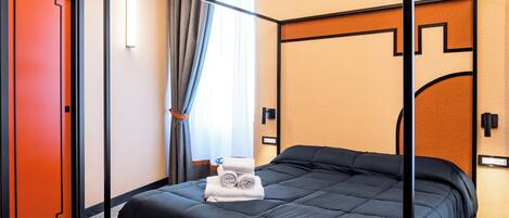 Una cama con dosel de estructura negra y colcha azul oscuro, una puerta roja y un espejo en la pared.