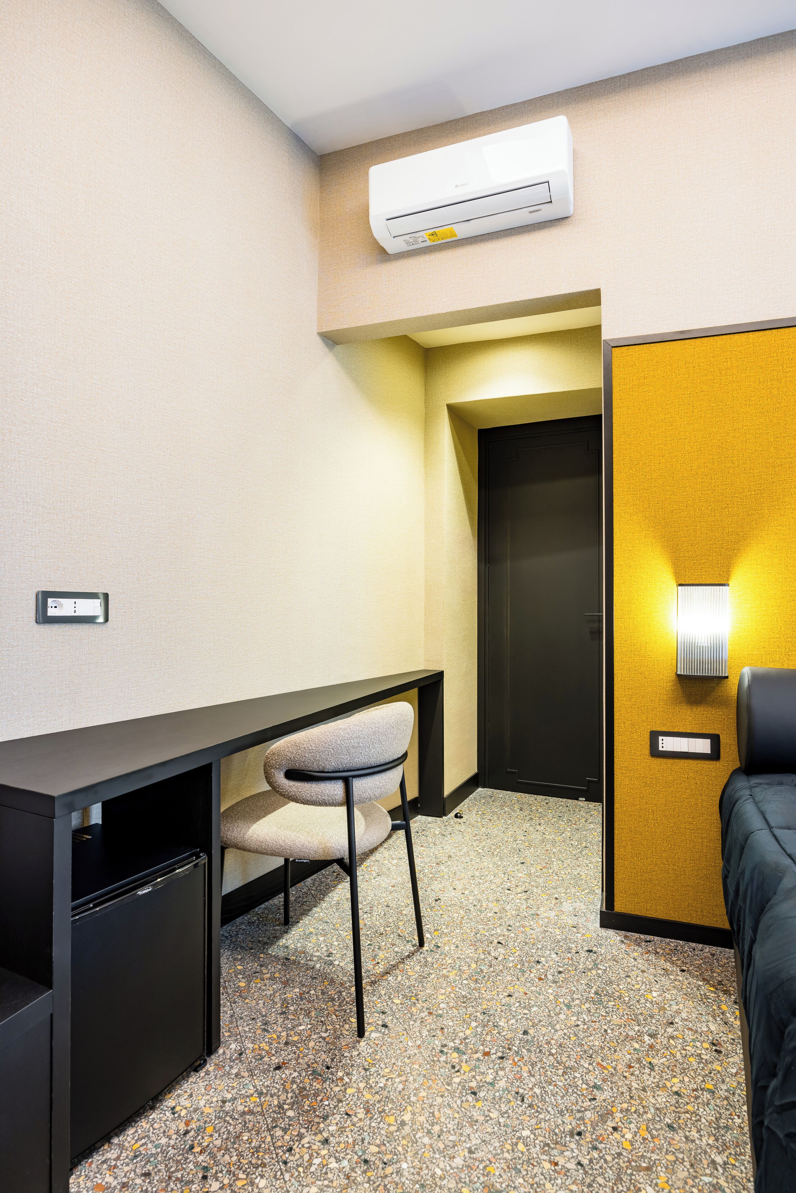 Hotellihuone, jossa on työpöytä, tuoli, sänky ja ilmastointilaite.