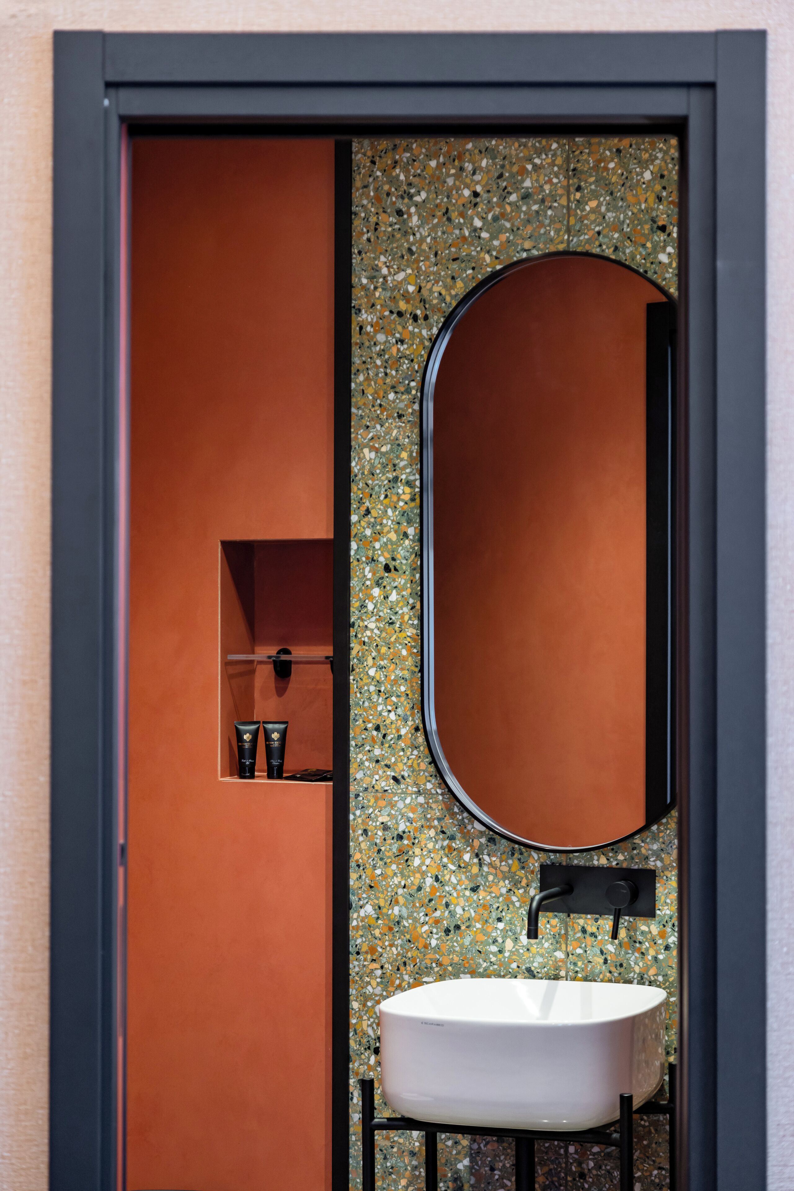 A bathroom with a white sink, a mirror, and toiletries in a shelf.