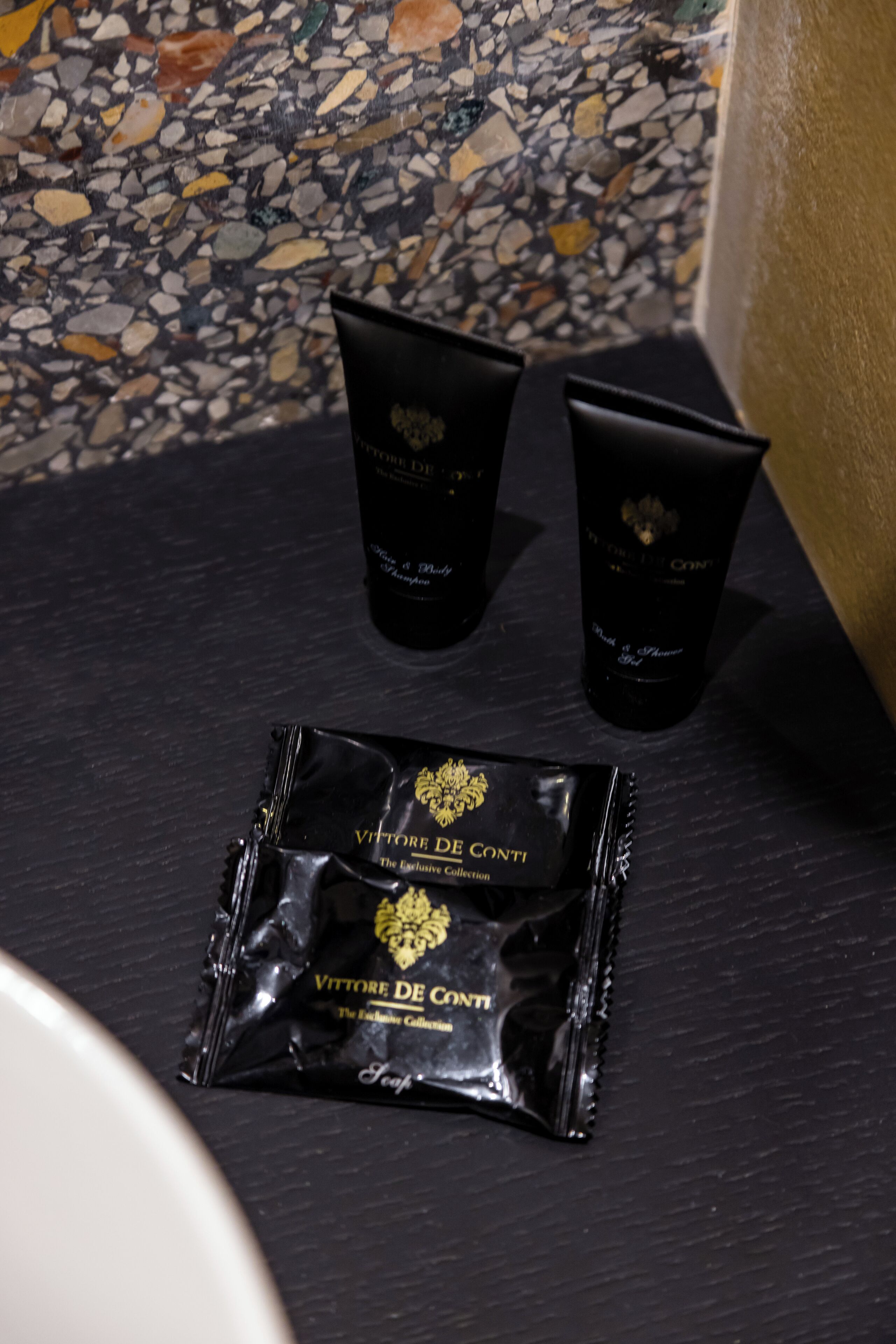 A bathroom with a black countertop, two black bottles, and a black packet on it.