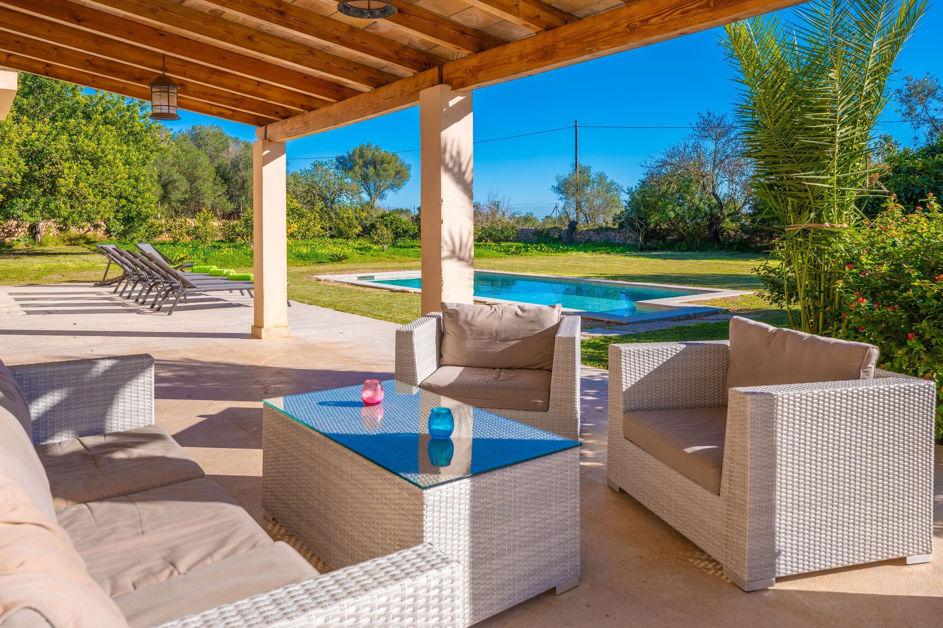 An outdoor patio with wicker furniture, a glass table, and a view of a swimming pool.
