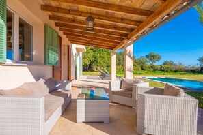 An outdoor patio with wicker furniture, a glass coffee table, and a view of a swimming pool. - Ses Set Tanques De Son Fosquet (Llucmajor)