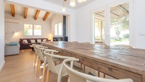 A spacious dining area with a long wooden table and several chairs, a sofa, and a large window providing natural light. - Ses Set Tanques De Son Fosquet (Llucmajor)