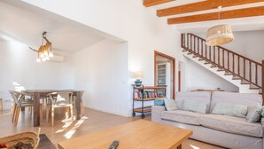 A spacious living room with a wooden coffee table, a sofa, a dining area with chairs, a staircase, and a bookshelf. - Ses Set Tanques De Son Fosquet (Llucmajor)