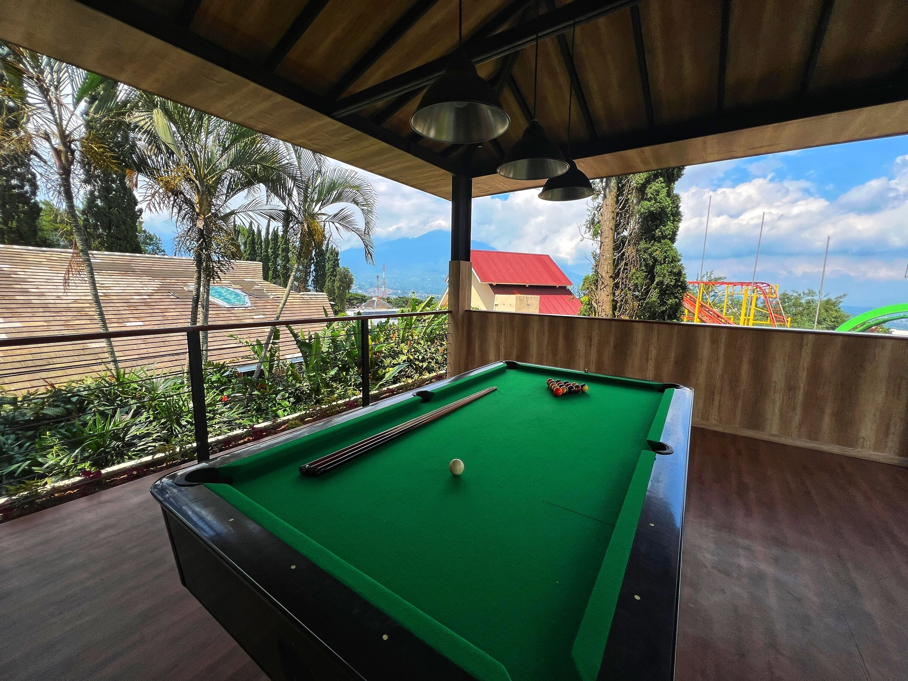 A pool table with a green felt surface, surrounded by a wooden deck and a metal railing.