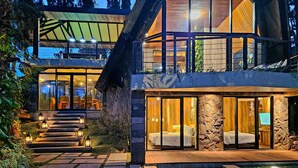 Una casa moderna de dos plantas con fachada de piedra, amplias ventanas y un espacio exterior luminoso con escalones que conducen a una piscina.