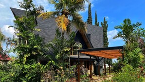 Un edificio moderno con techo inclinado, rodeado de exuberante vegetación tropical y un camino pavimentado.