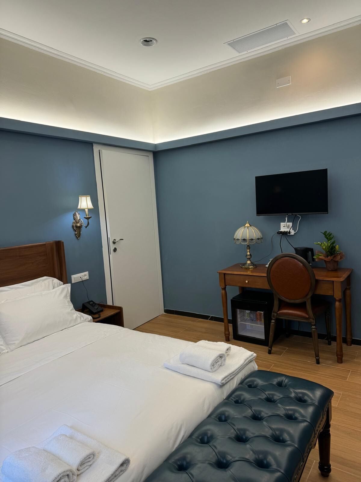 A hotel room with a bed, a desk, a chair, a television, and a lamp.