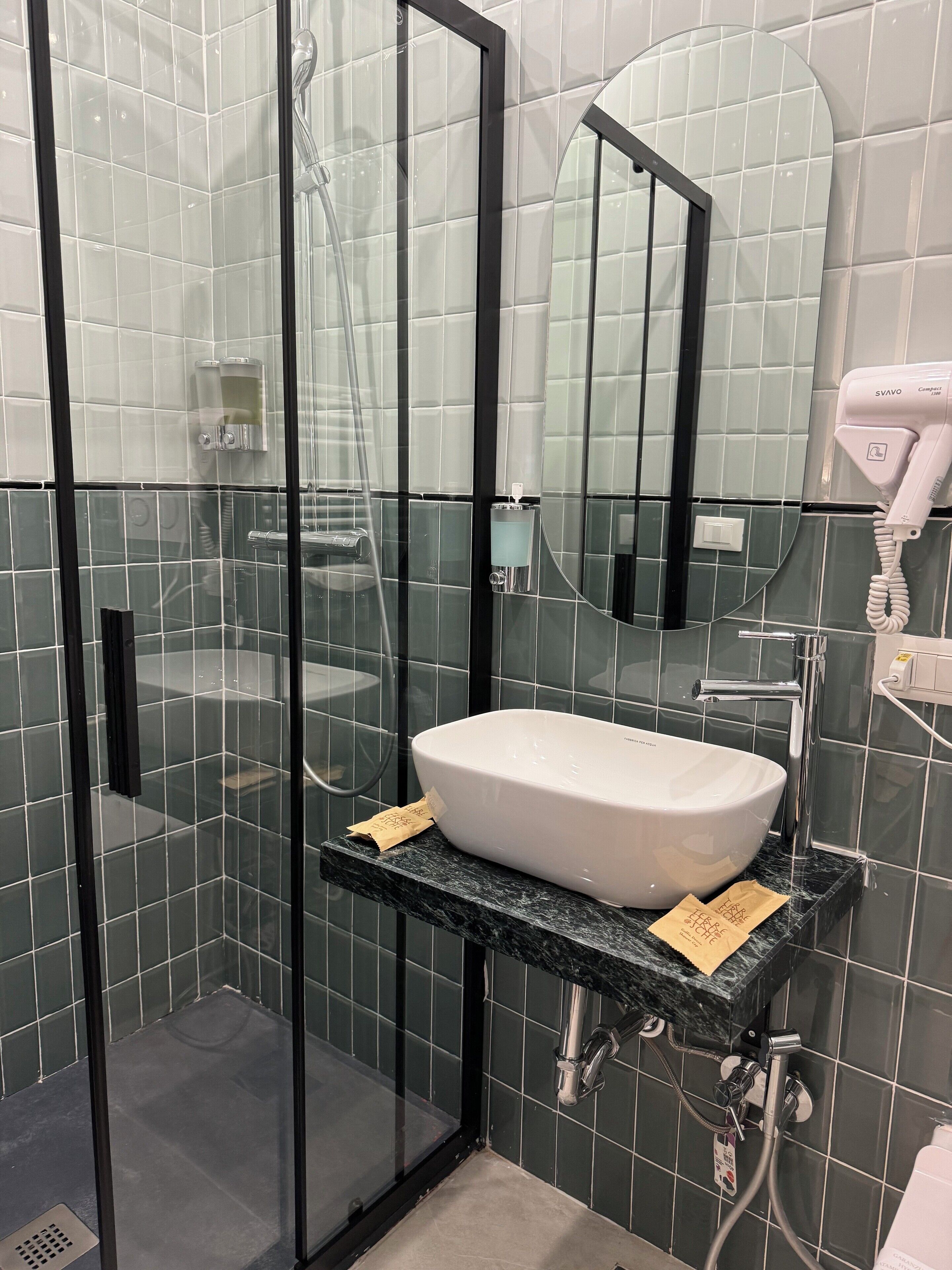 A modern bathroom with a glass-enclosed shower, a white sink, and a compact hairdryer.