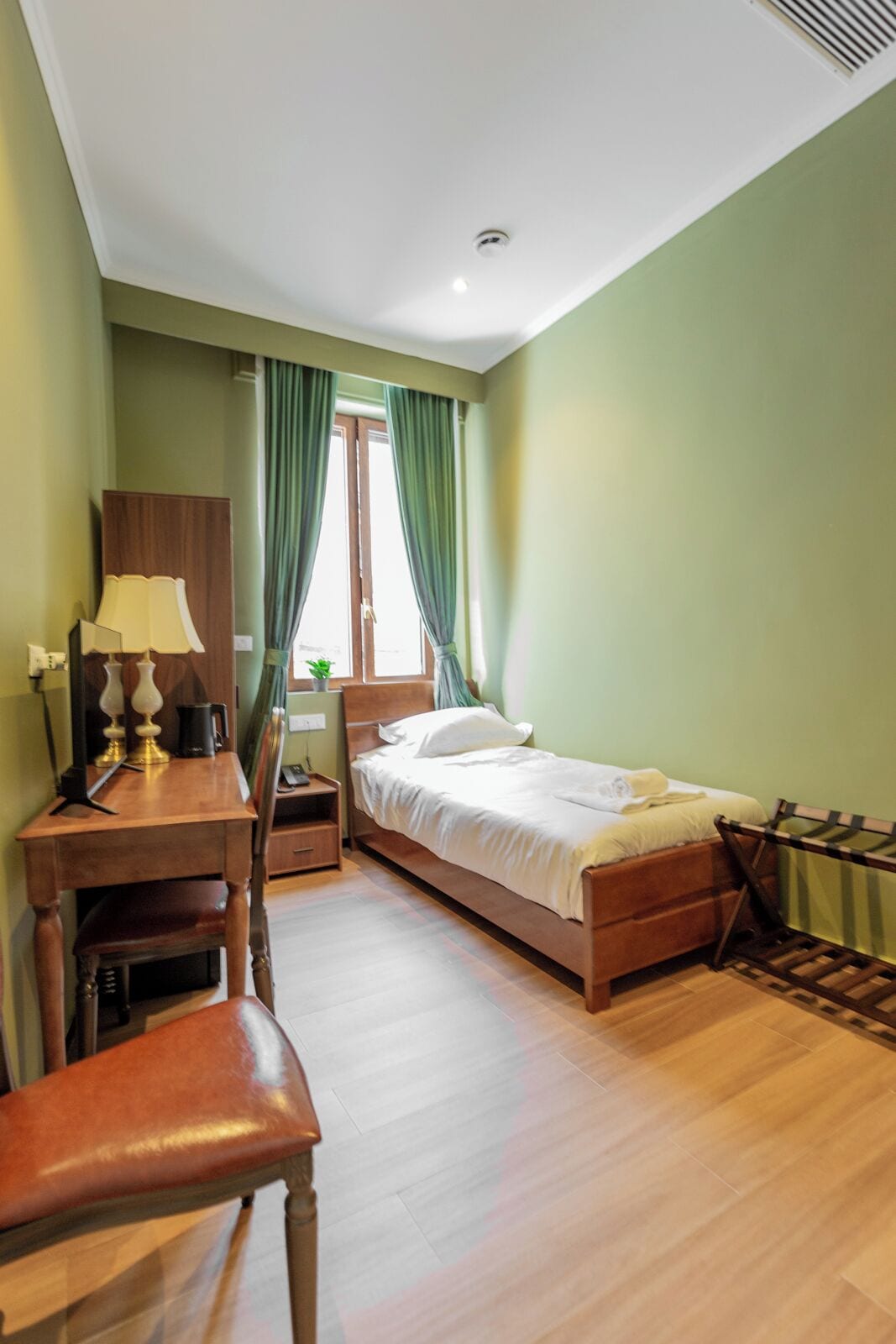 Een hotelkamer met een bed, bureau, stoel en een raam met gordijnen.