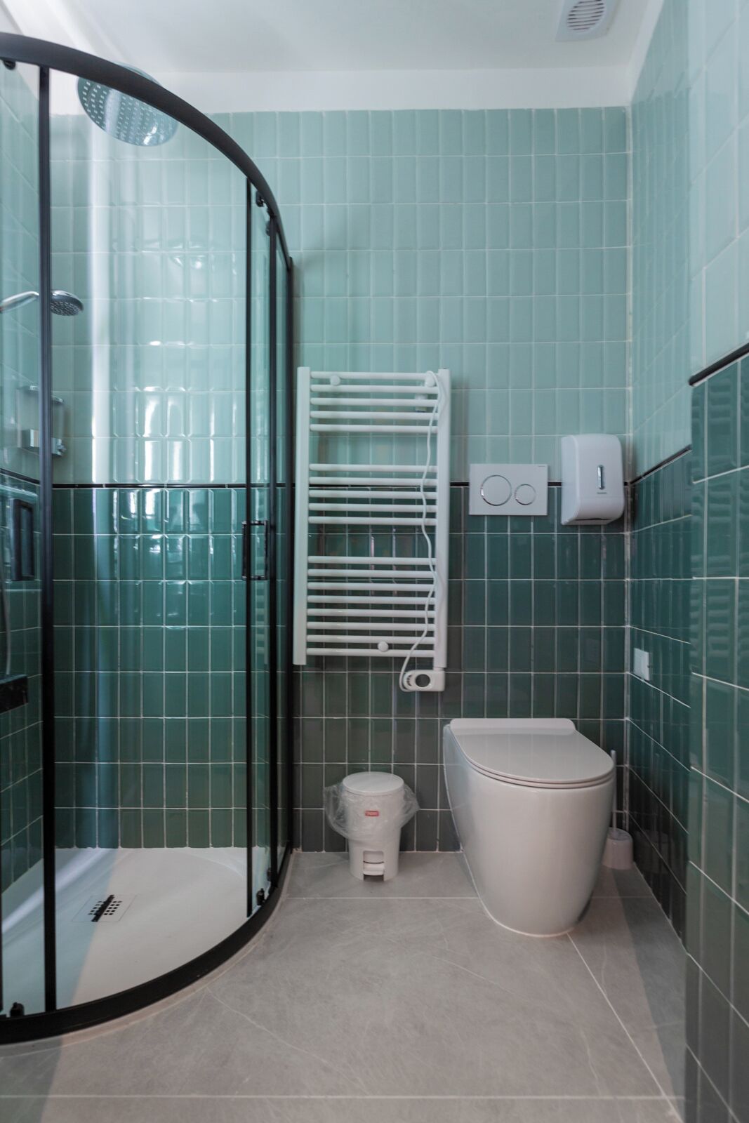 Une salle de bain avec une douche à parois de verre, des toilettes blanches, un porte-serviettes et un sèche-mains.
