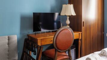 A hotel room with a wooden desk, a television, a leather chair, a grey sofa, and a wooden wardrobe.