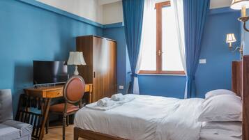 A hotel room with a bed, a desk with a TV, a chair, a wardrobe, and a window with curtains.