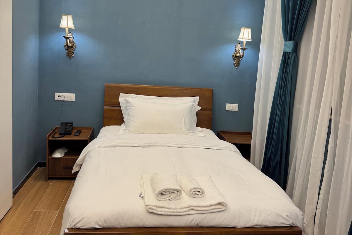 Una cama bien tendida con sábanas blancas, un cabecero de madera y dos mesitas de noche con lámparas.