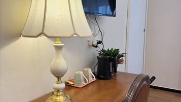 Een houten bureau met een lamp, een potplant en een dienblad met bekers en een boek. Een flatscreen televisie is aan de muur bevestigd.