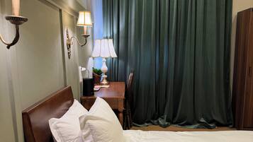 Quarto de hotel com cama, mesas de cabeceira, luminárias, escrivaninha e cortina.