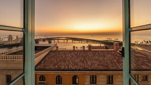 A view from a window overlooking a coastal area with a bridge, buildings with tiled roofs, and a calm sea.