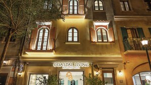 A hotel facade with a sign reading "COASTAL LIVING BOUTIQUE HOTEL," large windows, and potted plants at the entrance.