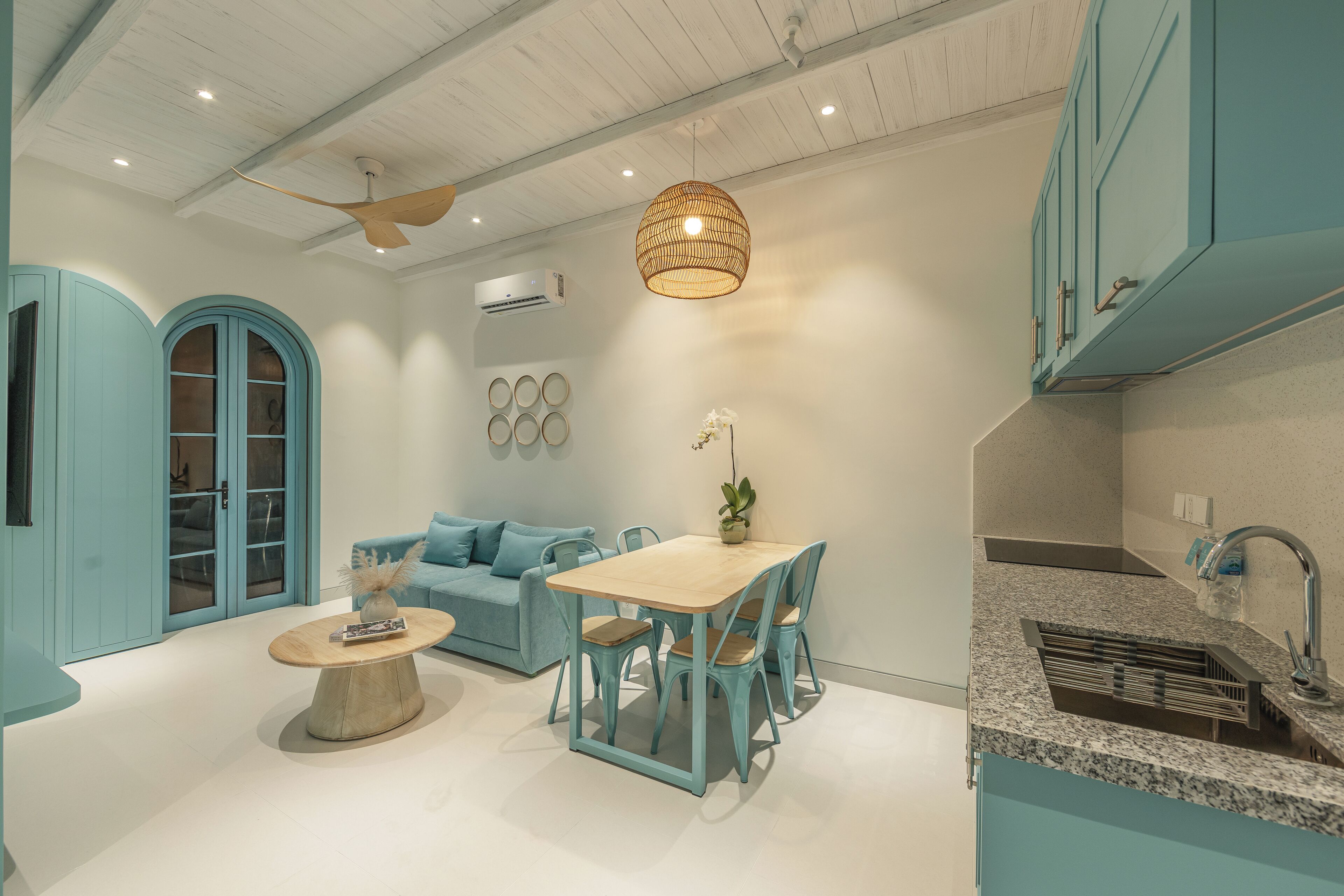 Una cocina moderna con armarios azul verdoso, encimera de granito y comedor con mesa y sillas de madera.