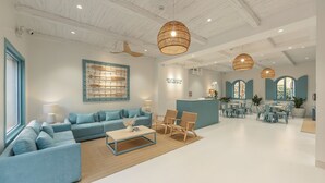 A spacious hotel lobby with a blue sofa, wicker chairs, a reception desk, and a large window with a view.
