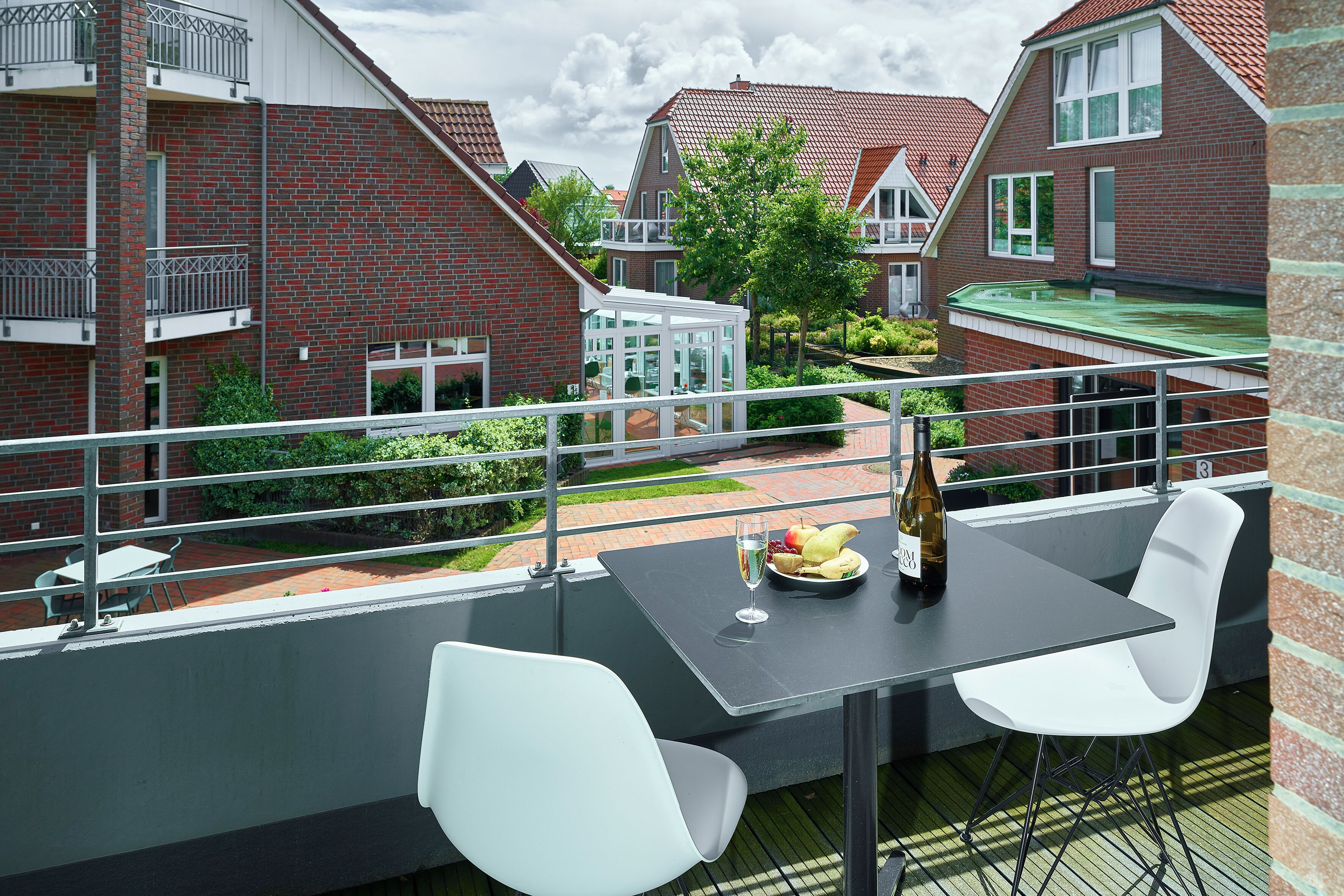 Un balcon avec une table, deux chaises, une bouteille et une assiette de fruits.