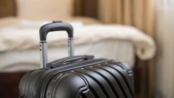 A black suitcase with a handle and wheels in a hotel room with a bed and curtains.