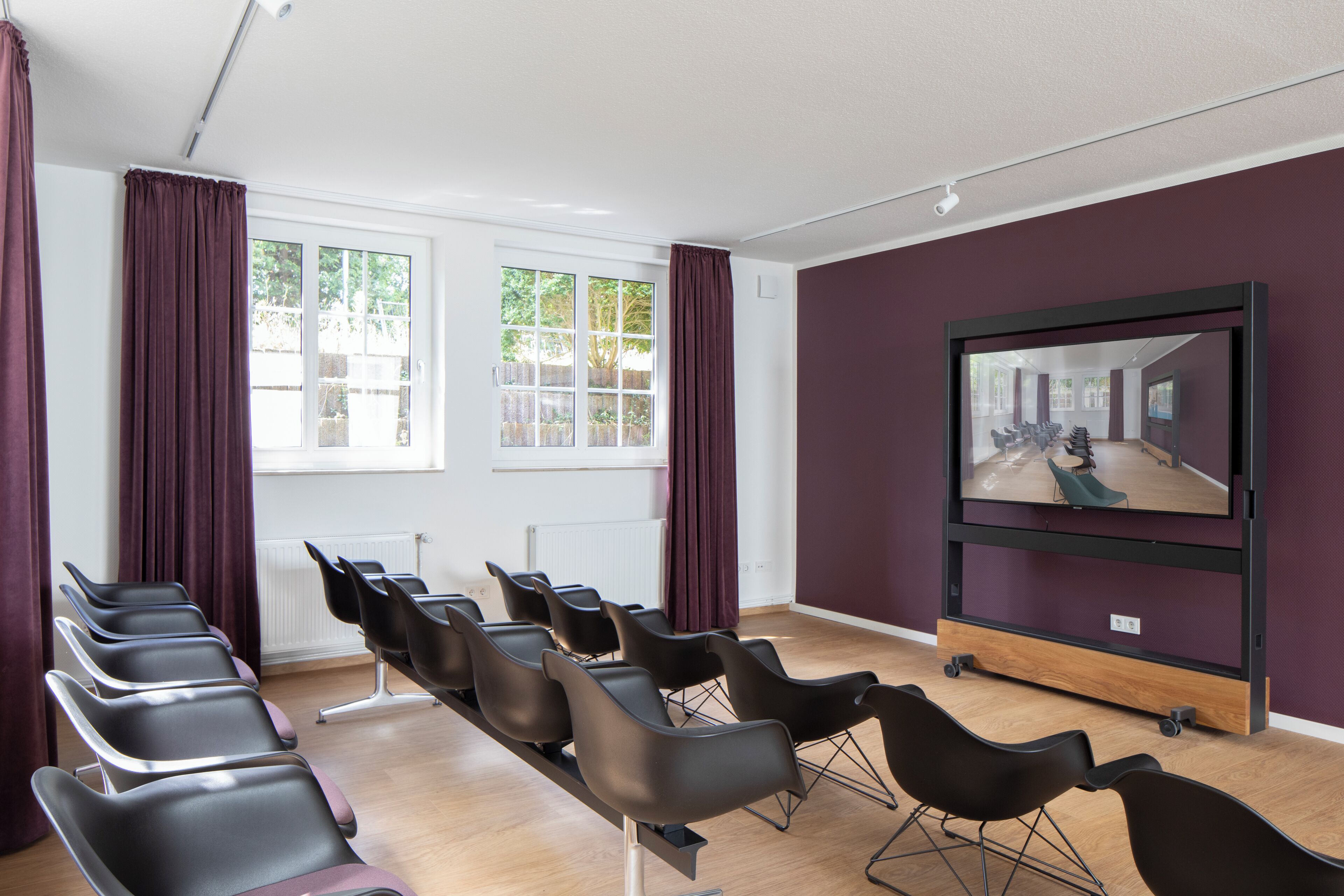 A conference room with rows of chairs, a large screen, and windows with curtains.