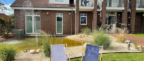 Una casa de dos pisos con fachada de ladrillo, un estanque pequeño y dos sillones de descanso en el jardín delantero.