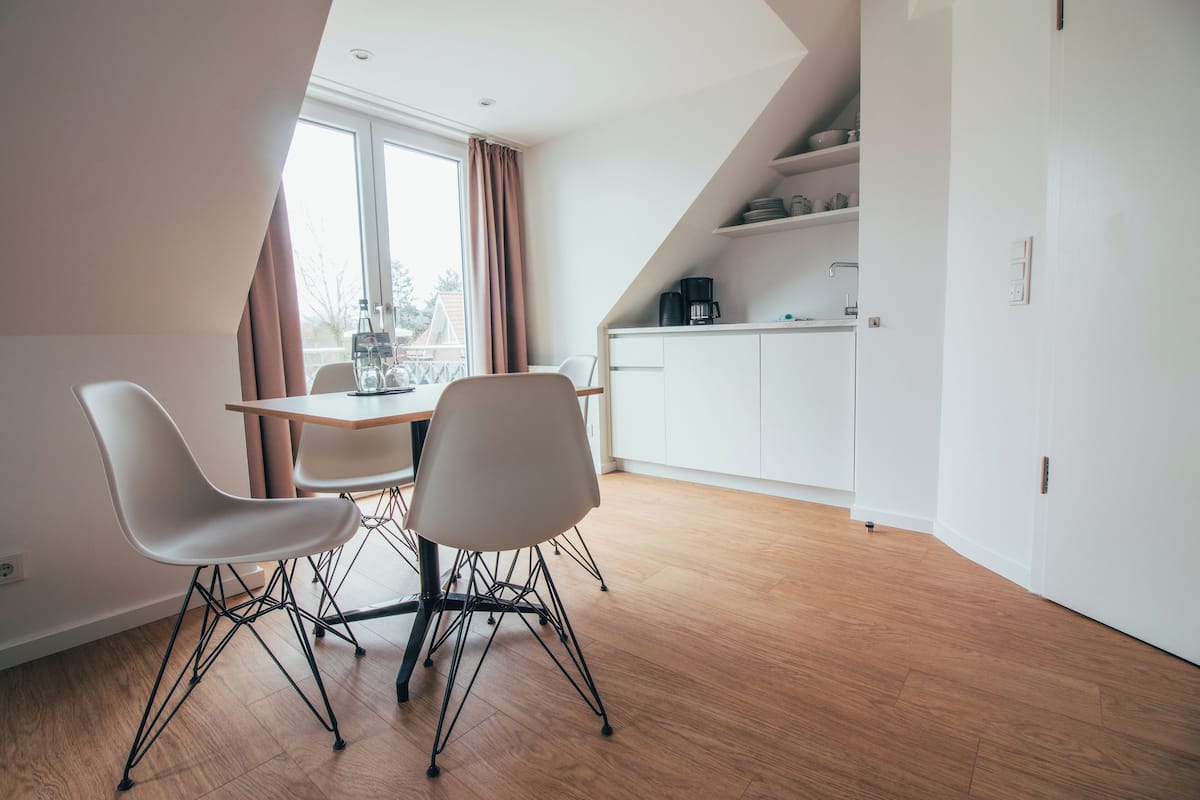 A modern kitchen with white cabinets, a coffee maker, and a dining area with a table and chairs.
