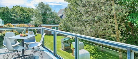 A deck with a table and chairs, overlooking a well-maintained lawn and trees.