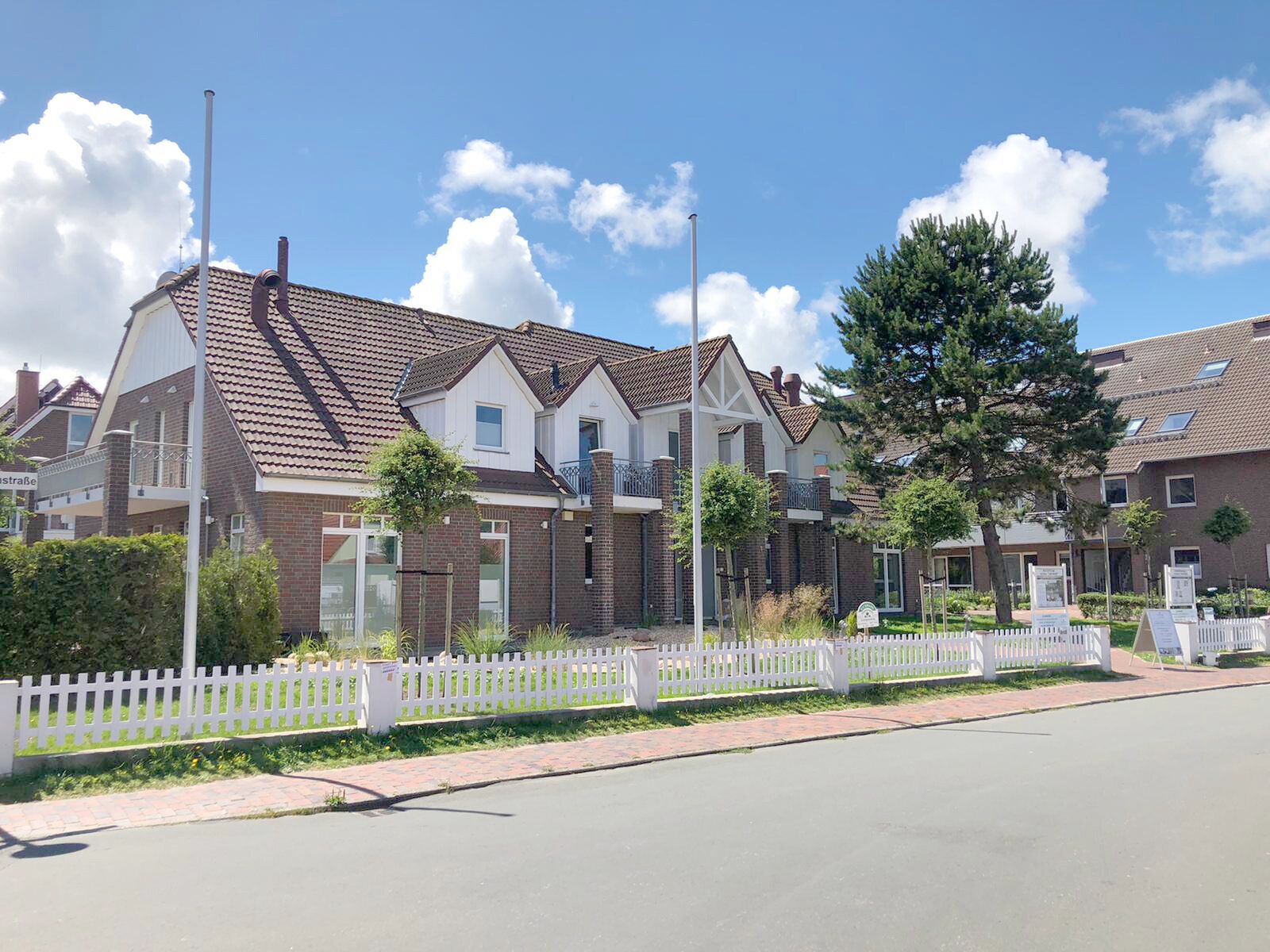 A row of modern two-story houses with brick facades, a white picket fence, and a clear sky.
