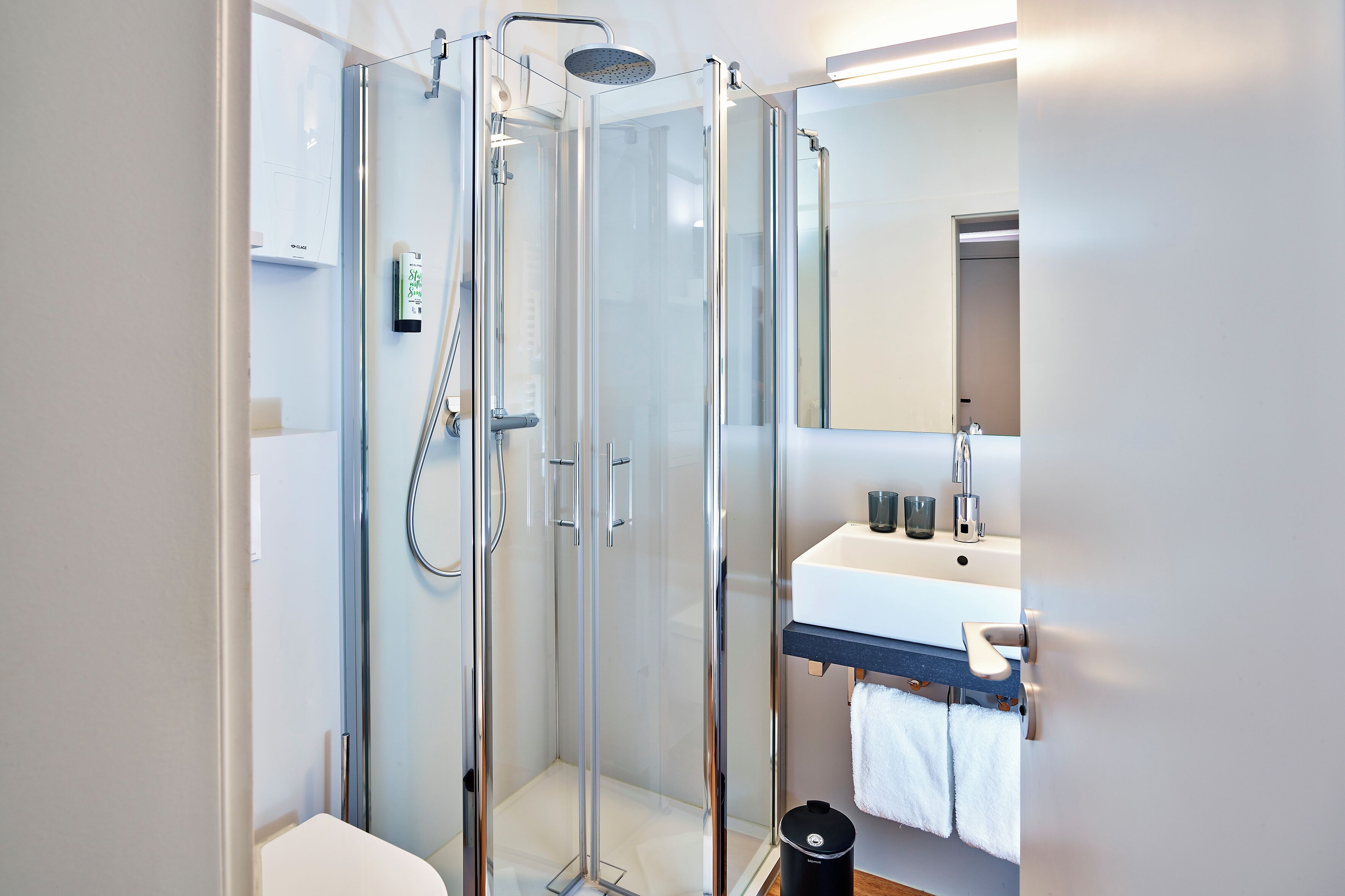 A modern bathroom with a glass-enclosed shower, a white sink, and a mirror above the sink.