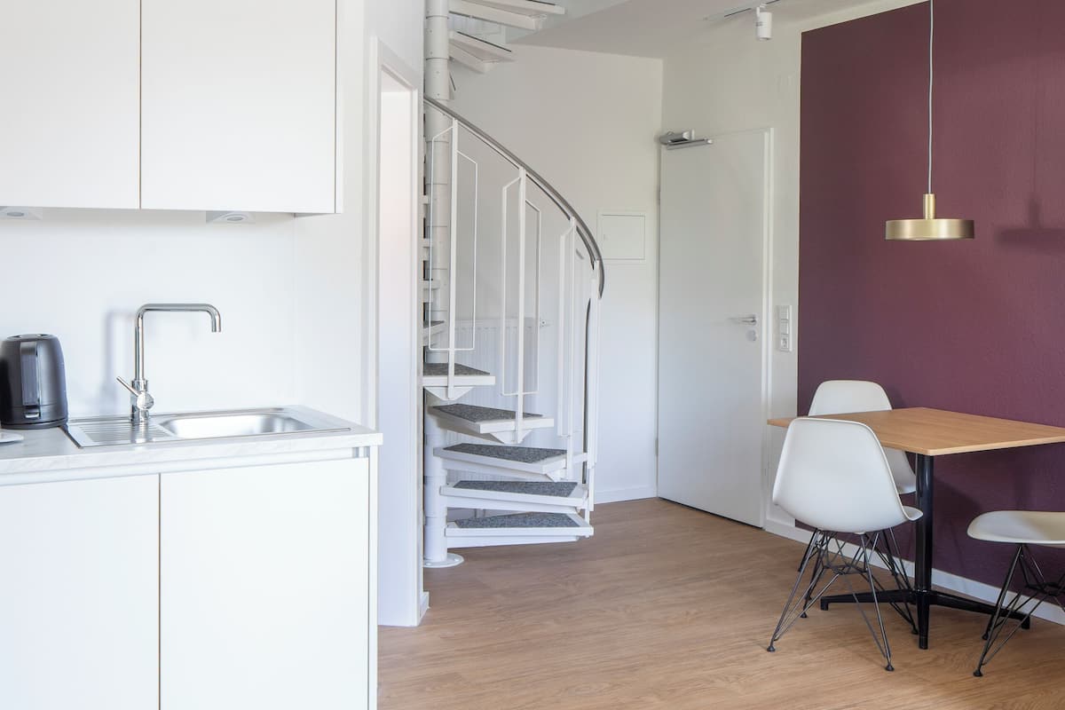A modern kitchen with white cabinets, a stainless steel sink, and a staircase leading to an upper level.