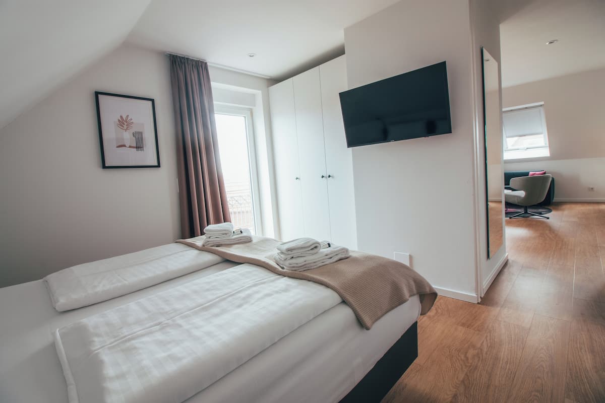 A modern hotel room with a large bed, a TV mounted on the wall, and a view of the hallway.