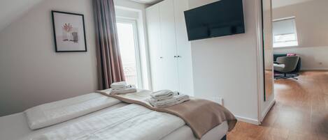 A modern hotel room with a large bed, a TV mounted on the wall, and a view of the hallway.