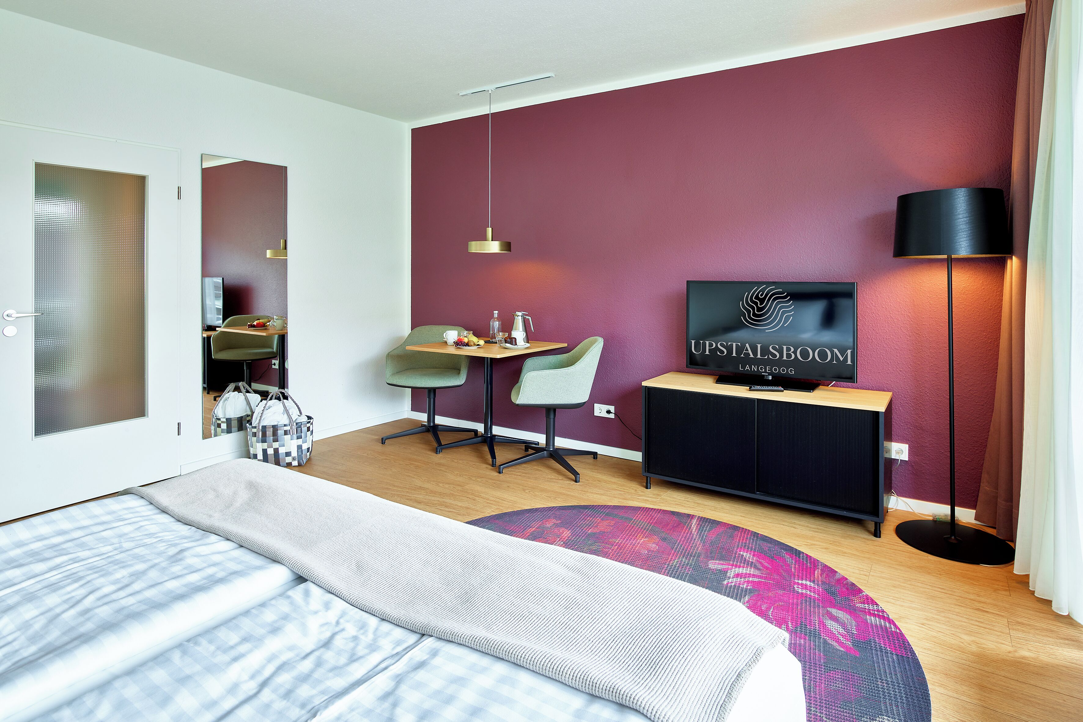 A modern hotel room with a bed, a desk, a chair, a TV, and a lamp.