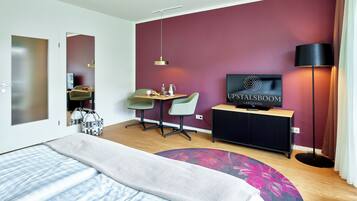 A modern hotel room with a bed, a desk, a chair, a TV, and a lamp.