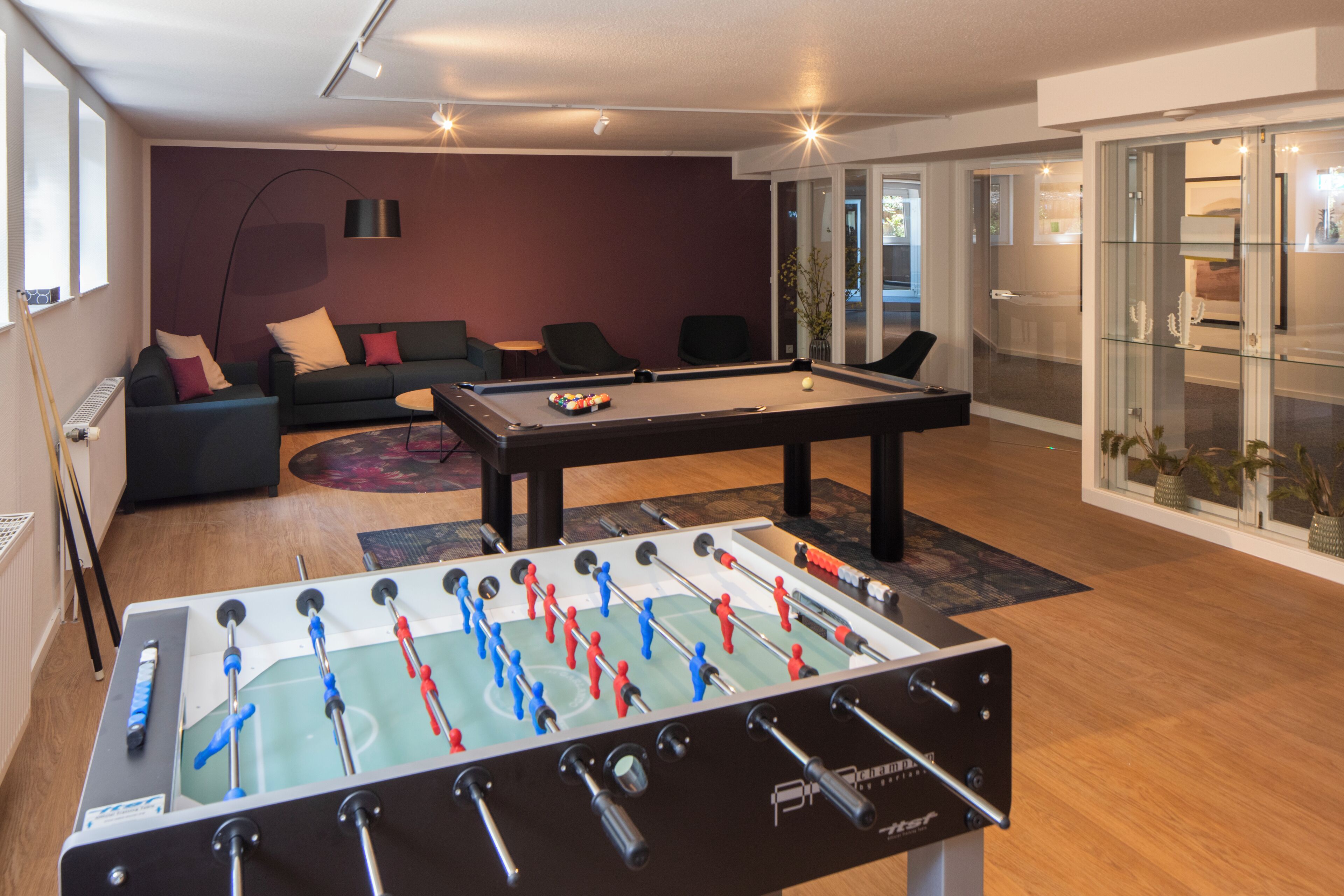 A room with a foosball table, a sofa, and a pool table.