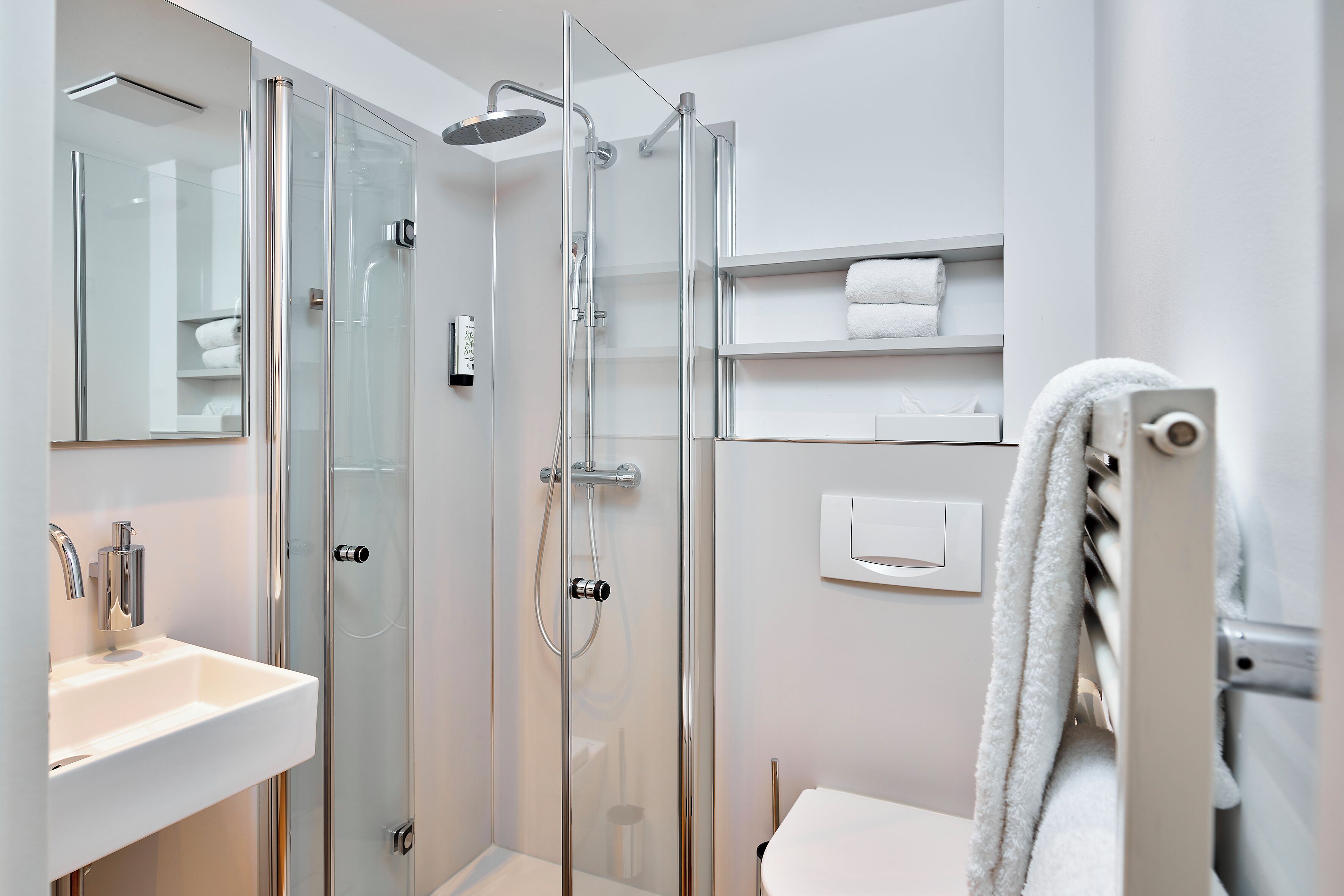 Un baño moderno con ducha de vidrio, lavamanos blanco y retrete.