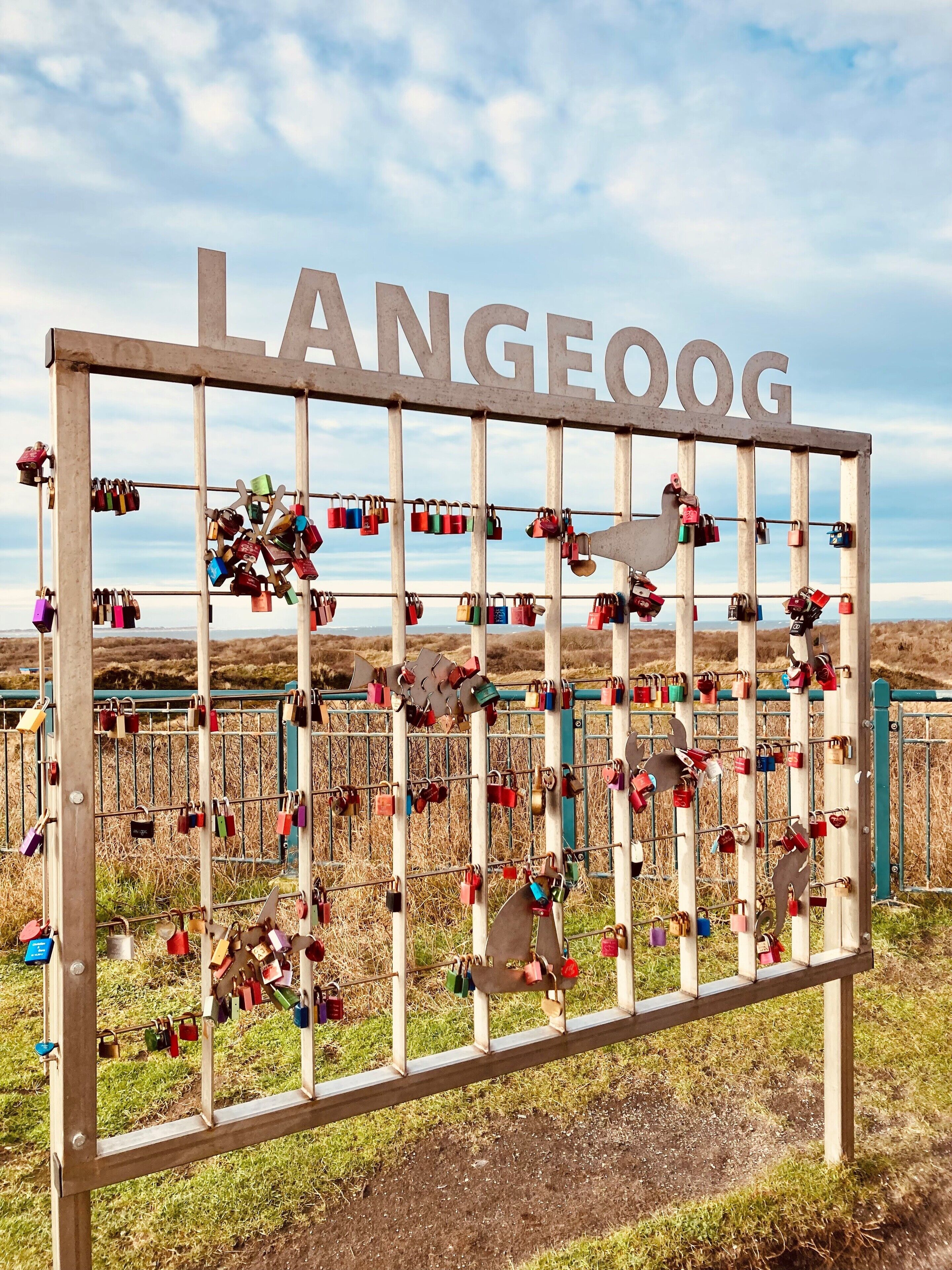 Un letrero con la palabra 'LANGEOOG' y una cerca metálica con numerosos candados.