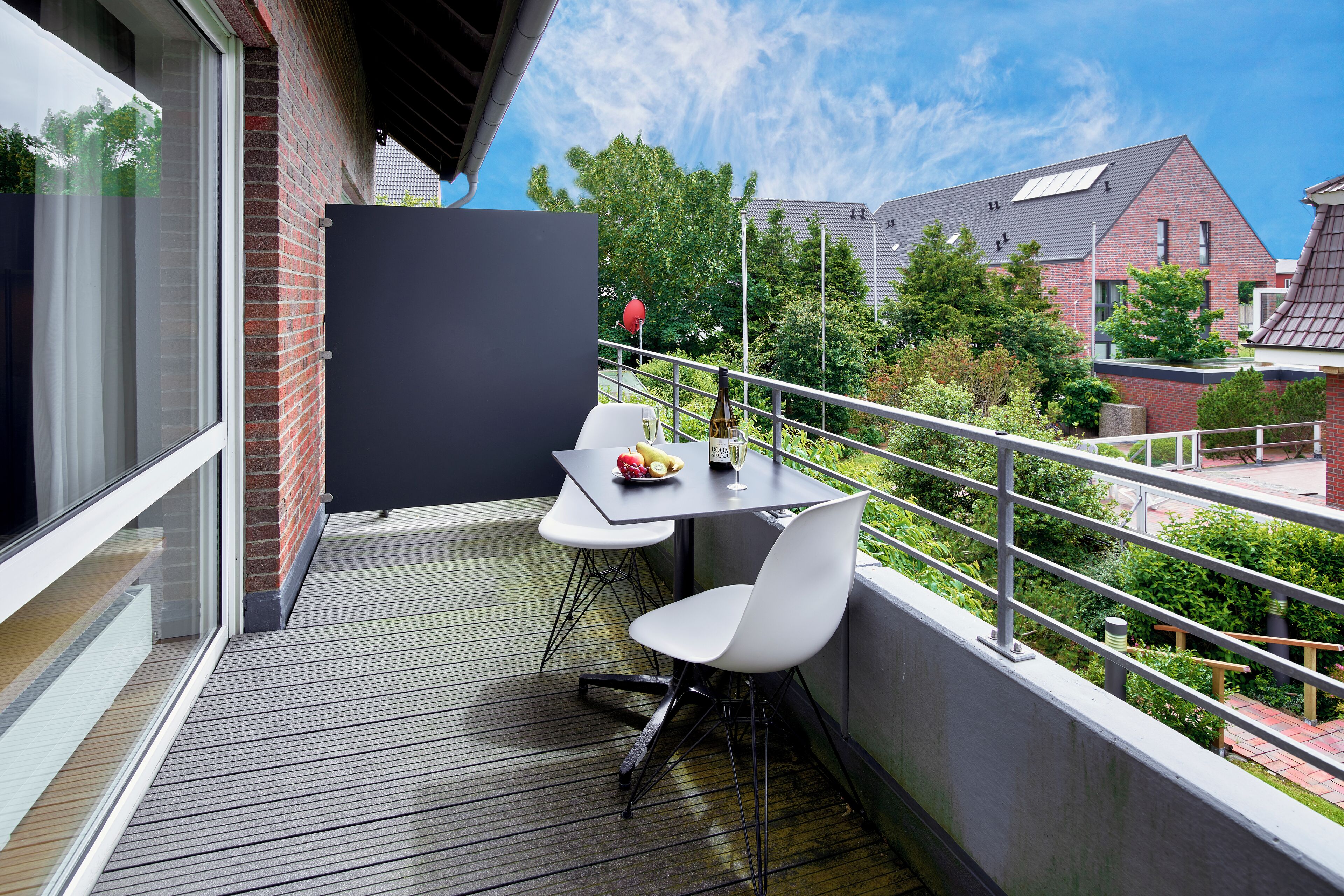 Ein Balkon mit Tisch, Stühlen, einer Flasche und einer Schüssel mit Obst.