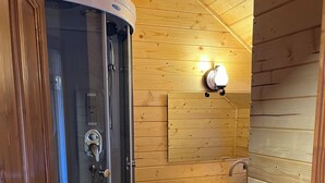A wooden cabin bathroom with a glass-enclosed shower, a sink, and a wooden shelf. - Pensiunea Vânătorul (Damuc)