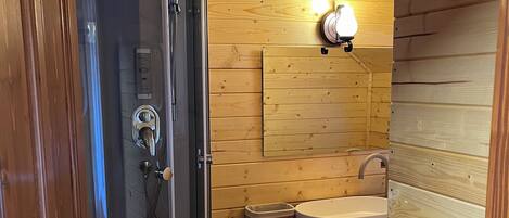 A wooden cabin bathroom with a glass-enclosed shower, a sink, and a wooden shelf.