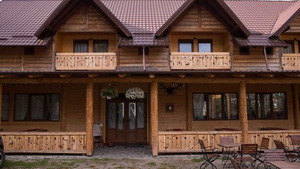 A wooden lodge with a balcony, large windows, and a stone-paved entrance. - Pensiunea Vânătorul (Damuc)