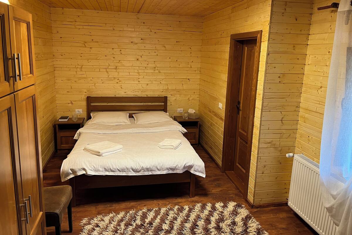 A wooden-paneled bedroom with a double bed, bedside tables, and a radiator.