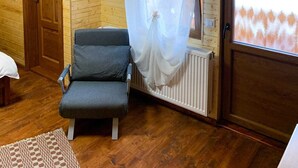 A wooden-paneled room with a grey sofa, a wooden door, a window with a sheer curtain, and a radiator. - Pensiunea Vânătorul (Damuc)