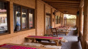 A covered outdoor seating area with wooden benches and tables, a stone floor, and a wooden fence in the background. - Pensiunea Vânătorul (Damuc)