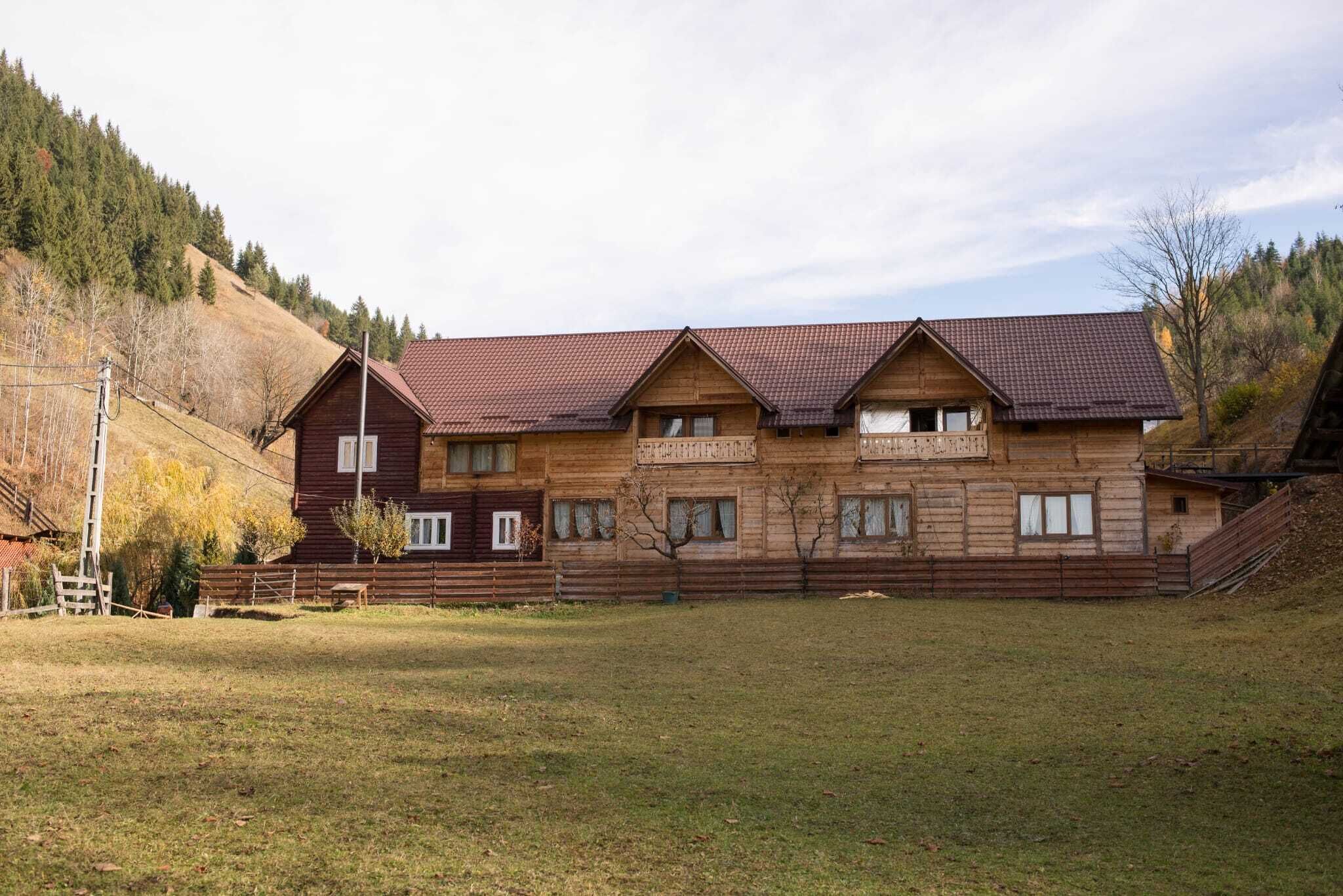 A wooden building with a sloped roof, multiple windows, and a fenced yard.
