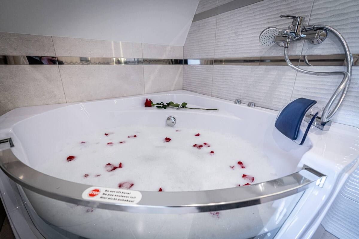 A modern bathroom with a large bathtub, a handheld showerhead, and rose petals floating in the water.